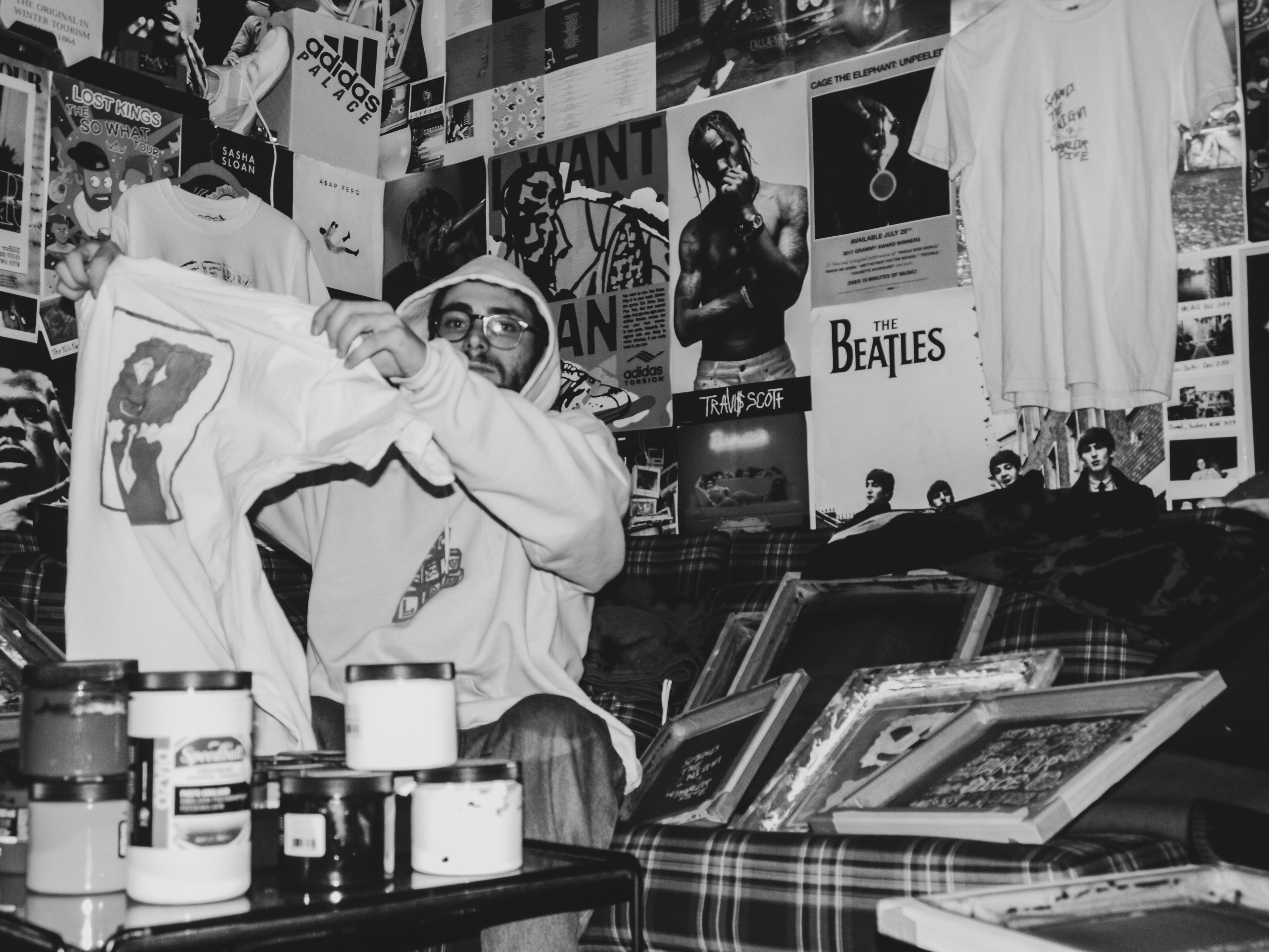 Phil Deutsch waving a printed Graphic Tee, surrounded by screens and band posters. Black and White Image